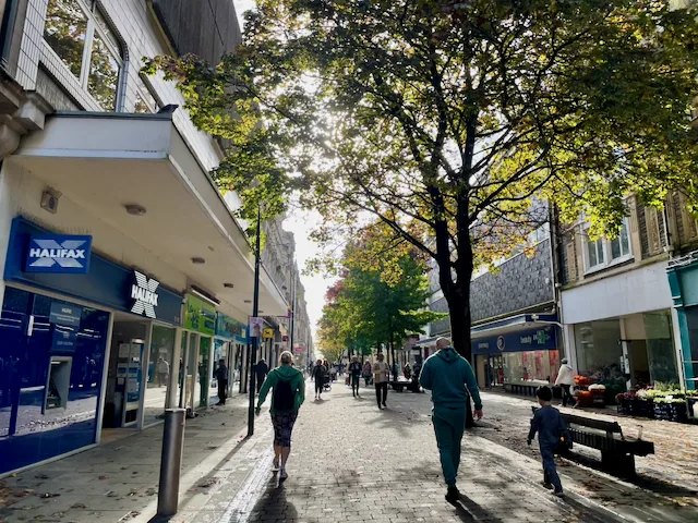 People walk along a tree-lined pedestrian street in Newport city centre.