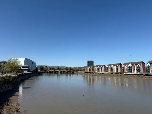 The River Usk in Newport on a clear day with buildings and a bridge in the distance.